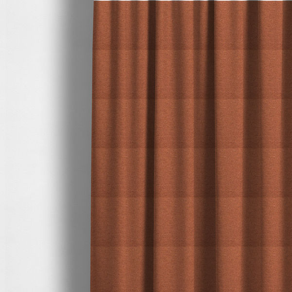 The fabric used to create these made-to-measure curtains is a deep rust or burnt orange textile with a dense diagonal twill weave. The fabric features a rich, multi-tonal blend of saturated orange yarns interlaced with darker brown and subtle flecks of green or gold, giving it a heathered, earthy depth.