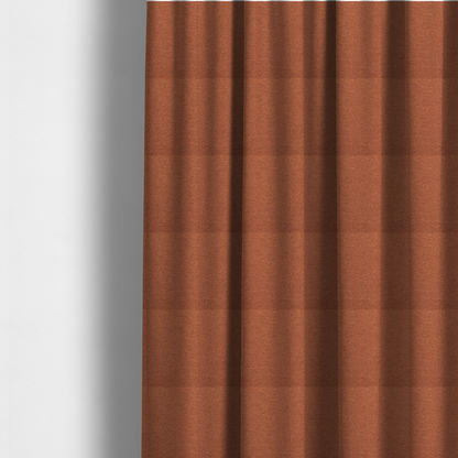 The fabric used to create these made-to-measure curtains is a deep rust or burnt orange textile with a dense diagonal twill weave. The fabric features a rich, multi-tonal blend of saturated orange yarns interlaced with darker brown and subtle flecks of green or gold, giving it a heathered, earthy depth.