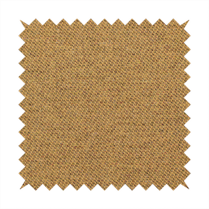 A golden mustard or ochre textile featuring a dense diagonal twill weave. The fabric is a multi-tonal blend, interlacing warm yellow-gold yarns with subtle flecks of darker brown and charcoal, creating a rich, heathered depth.