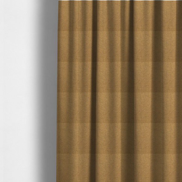 The fabric used to create these made-to-measure curtains is a golden mustard or ochre textile featuring a dense diagonal twill weave. The fabric is a multi-tonal blend, interlacing warm yellow-gold yarns with subtle flecks of darker brown and charcoal, creating a rich, heathered depth.