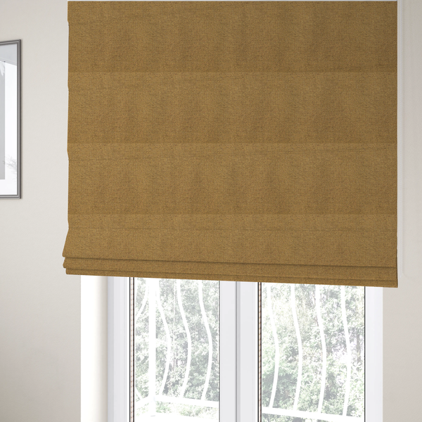 The fabric used to create these Roman blinds is a golden mustard or ochre textile featuring a dense diagonal twill weave. The fabric is a multi-tonal blend, interlacing warm yellow-gold yarns with subtle flecks of darker brown and charcoal, creating a rich, heathered depth.