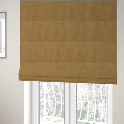 The fabric used to create these Roman blinds is a golden mustard or ochre textile featuring a dense diagonal twill weave. The fabric is a multi-tonal blend, interlacing warm yellow-gold yarns with subtle flecks of darker brown and charcoal, creating a rich, heathered depth.
