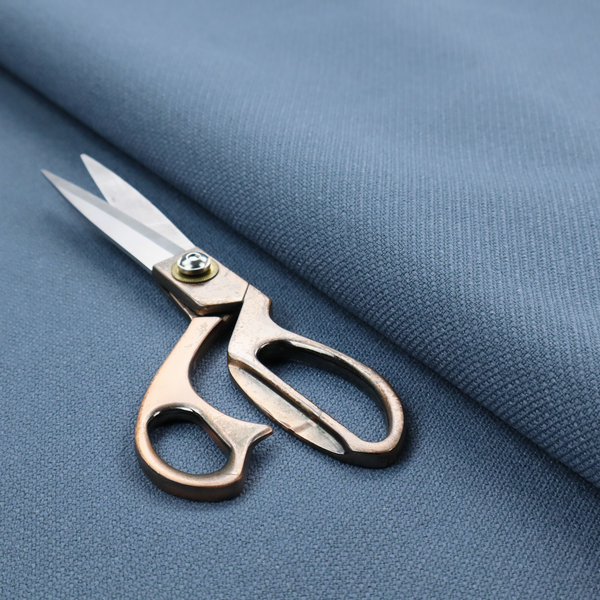A medium denim or cornflower blue textile featuring a tight diagonal twill weave. The fabric is woven with a blend of soft blue and muted grey-blue yarns, creating a calm, uniform colour profile with subtle tonal depth.