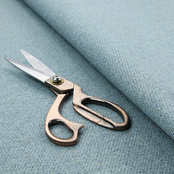 A dusty aqua or pale teal textile featuring a tight diagonal twill weave. The fabric is a multi-tonal blend, interlacing soft blue-green yarns with subtle flecks of grey and pale gold, creating a sophisticated, heathered depth.