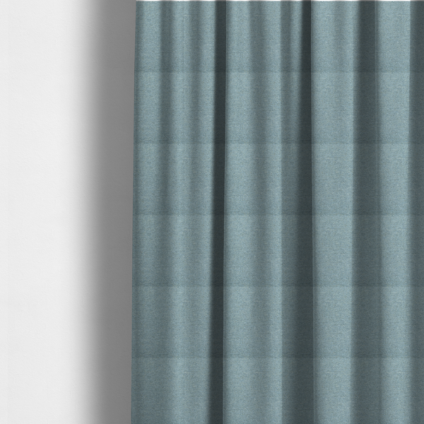 The fabric used to create these made-to-measure curtains is a dusty aqua or pale teal textile featuring a tight diagonal twill weave. The fabric is a multi-tonal blend, interlacing soft blue-green yarns with subtle flecks of grey and pale gold, creating a sophisticated, heathered depth.