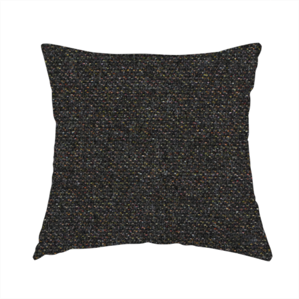 The fabric used to create this handmade cushion is a near-black charcoal base heavily flecked with multi-coloured yarns in gold, rust, and grey.
