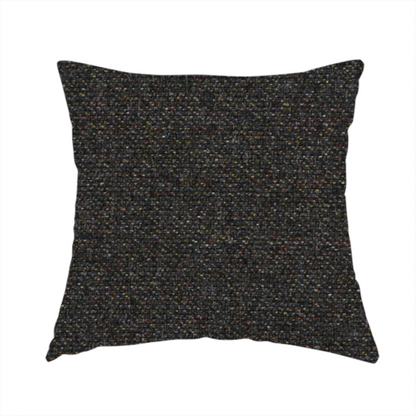The fabric used to create this handmade cushion is a near-black charcoal base heavily flecked with multi-coloured yarns in gold, rust, and grey.