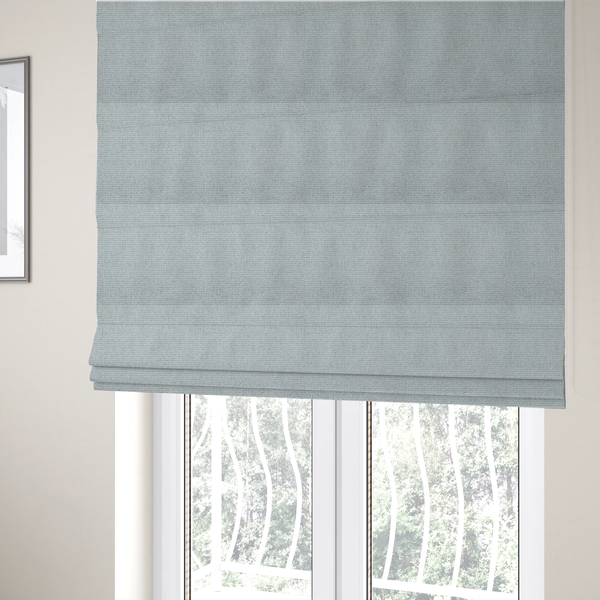 The fabric used to create these Roman blinds is a very light ice-grey or tinted white fabric featuring a distinct, tightly woven grid texture. The material showcases a multi-tonal, basket-weave style pattern with blended pale silver and crisp off-white threads, creating a bright, minimalist, and matte finish across the entire surface.