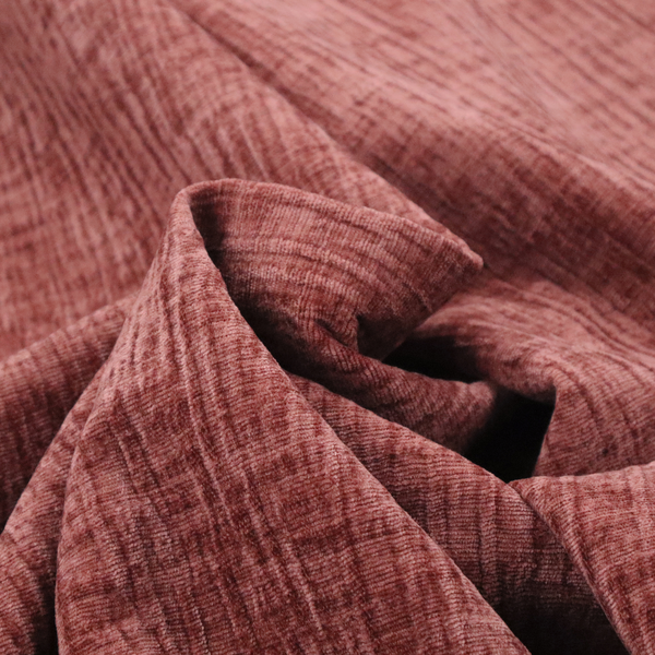 A textured upholstery fabric in a dusty rose or terracotta pink colour. The fabric features a raised, cross-hatched slub texture with subtle vertical and horizontal ridges, giving it a cosy, slightly distressed chenille appearance.