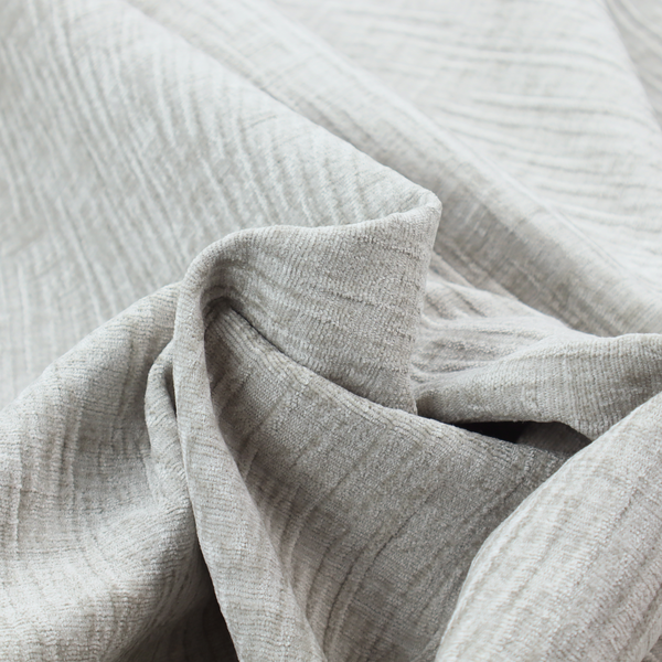 A textured upholstery fabric in a light silver or pale grey colour. The material features a subtle cross-hatched slub texture with fine vertical and horizontal ridges, creating a soft, dimensional chenille finish.