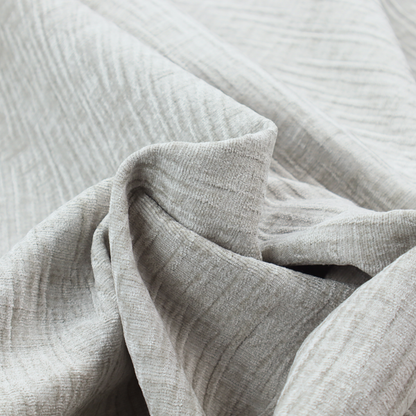 A textured upholstery fabric in a light silver or pale grey colour. The material features a subtle cross-hatched slub texture with fine vertical and horizontal ridges, creating a soft, dimensional chenille finish.