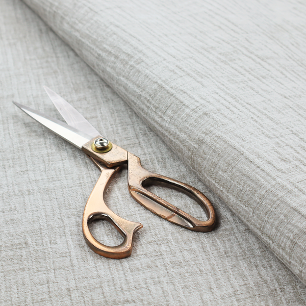 A textured upholstery fabric in a light silver or pale grey colour. The material features a subtle cross-hatched slub texture with fine vertical and horizontal ridges, creating a soft, dimensional chenille finish.