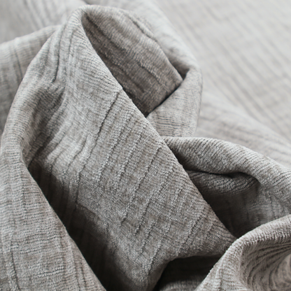 A textured upholstery fabric in a mid-tone grey or pebble shade. The material features a distinct cross-hatched slub texture with prominent vertical and fine horizontal ridges, creating a soft, dimensional chenille finish.
