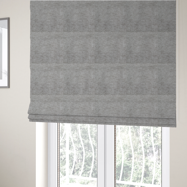 The fabric used to create these Roman blinds is a textured upholstery fabric in a mid-tone grey or pebble shade. The material features a distinct cross-hatched slub texture with prominent vertical and fine horizontal ridges, creating a soft, dimensional chenille finish.