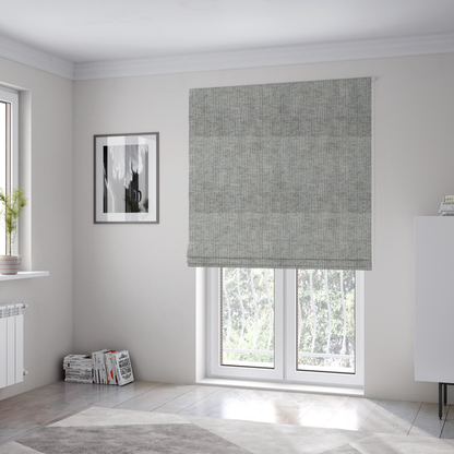The fabric used to create these Roman blinds is a textured upholstery fabric in a mid-tone grey or pebble shade. The material features a distinct cross-hatched slub texture with prominent vertical and fine horizontal ridges, creating a soft, dimensional chenille finish.