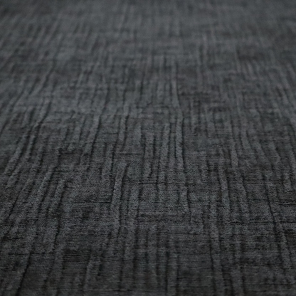 A textured upholstery fabric in a near-black or dark anthracite shade. The material features a distinct cross-hatched slub texture with prominent vertical and fine horizontal ridges, creating a soft, dimensional chenille finish.