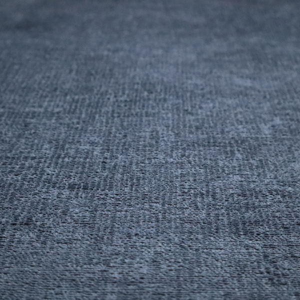 A textured fabric swatch in a deep slate blue or denim colour. The material features a dense, uniform nubby weave with subtle dark mottling throughout, giving the soft, textured surface a multi-tonal appearance.