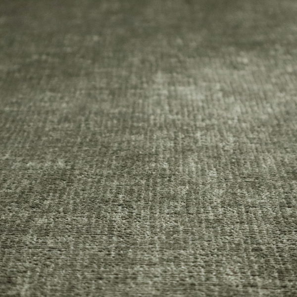 A textured fabric swatch in an earthy olive green or sage colour. The material features a dense, uniform nubby weave with subtle dark mottling throughout, giving the soft, textured surface a multi-tonal, organic appearance.