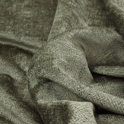 A textured fabric swatch in an earthy olive green or sage colour. The material features a dense, uniform nubby weave with subtle dark mottling throughout, giving the soft, textured surface a multi-tonal, organic appearance.