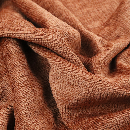 A textured fabric swatch in a rich rust or burnt sienna colour. The material features a dense, uniform nubby weave with subtle dark undertones and shading, giving the soft surface a multi-tonal, warm appearance.