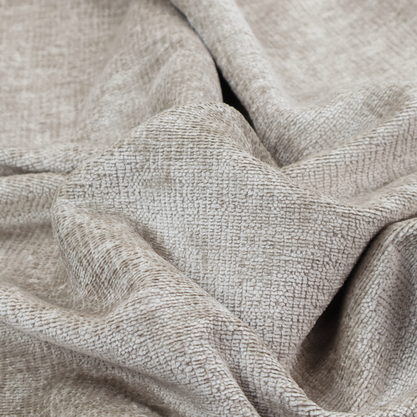 A textured fabric swatch in a light, neutral taupe or sandy beige colour. The material features a dense, uniform nubby weave with subtle horizontal striations and warm grey undertones, creating a soft, multi-tonal appearance.