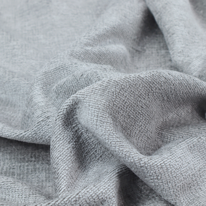 A textured fabric swatch in a cool, light-to-medium grey or stone colour. The material features a dense, uniform nubby weave with subtle horizontal shadowing, creating a soft, contemporary matte finish.