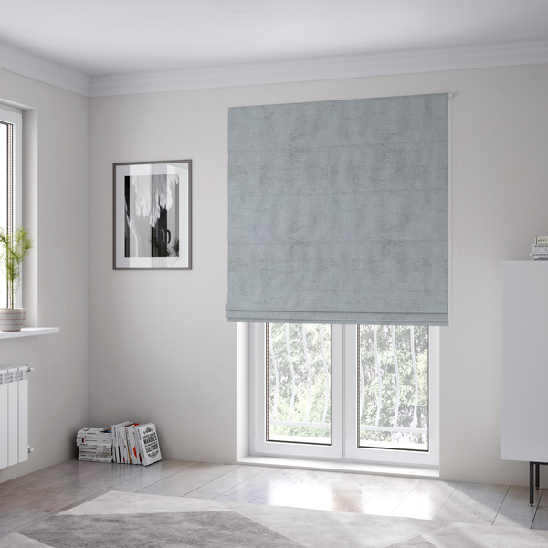 The fabric used to create these Roman blinds is a textured fabric swatch in a cool, light-to-medium grey or stone colour. The material features a dense, uniform nubby weave with subtle horizontal shadowing, creating a soft, contemporary matte finish.
