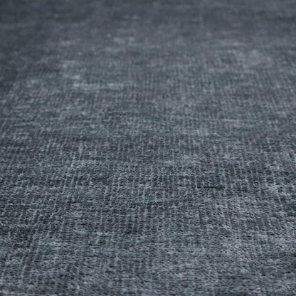 a textured fabric swatch in a dark charcoal or graphite grey colour. The material features a dense, uniform nubby weave with deep, moody undertones and subtle dark shadowing, creating a rich, contemporary appearance.