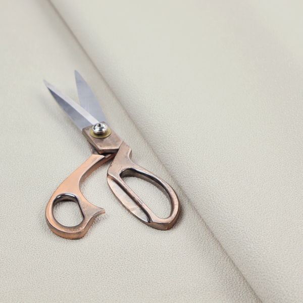 A light beige or off-white suede fabric. The textile features a highly detailed, dense, and uniform embossed pebbled pattern, giving the soft suede material an intricate, tactile texture reminiscent of shagreen.