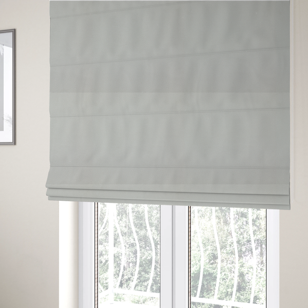 The fabric used to create these Roman blinds is a light grey Merida Suede upholstery fabric. The textile features a highly detailed, dense, and uniform embossed pebbled pattern, giving the soft grey suede material an intricate, tactile shagreen texture.