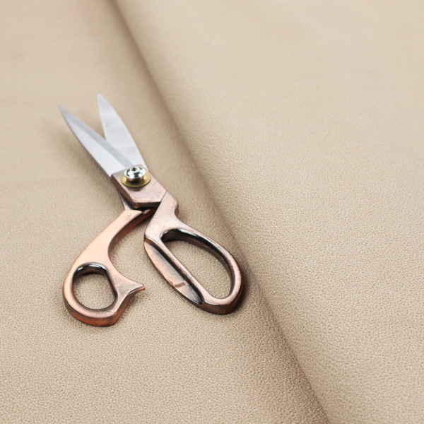 A warm beige or tan Merida Suede upholstery fabric. The textile features a highly detailed, dense, and uniform embossed pebbled pattern, giving the soft suede material an intricate, tactile shagreen texture.