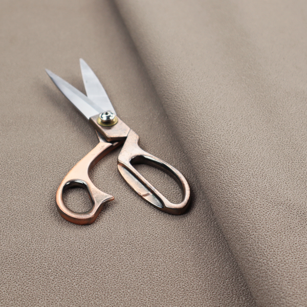 A taupe or dark beige Merida Suede upholstery fabric. The textile features a highly detailed, dense, and uniform embossed pebbled pattern, giving the soft suede material an intricate, tactile shagreen texture.