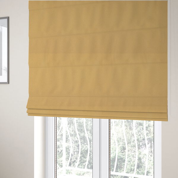 The fabric used to create these Roman blinds is a warm ochre or golden yellow Merida Suede upholstery fabric. The textile features a highly detailed, dense, and uniform embossed pebbled pattern, giving the soft suede material an intricate, tactile shagreen texture.