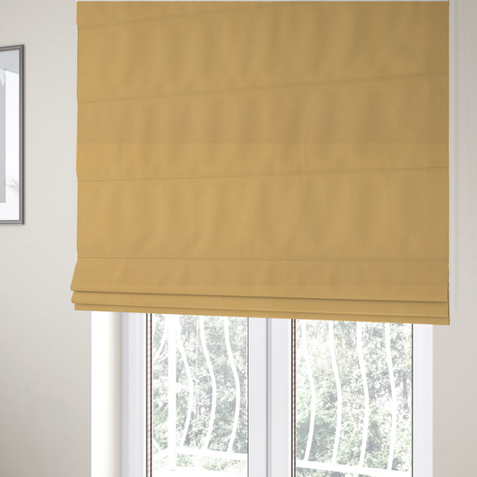 The fabric used to create these Roman blinds is a warm ochre or golden yellow Merida Suede upholstery fabric. The textile features a highly detailed, dense, and uniform embossed pebbled pattern, giving the soft suede material an intricate, tactile shagreen texture.