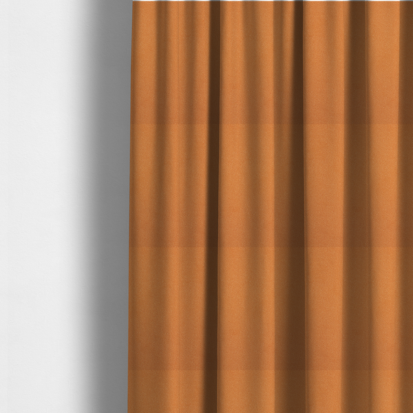 The fabric used to create these made-to-measure curtains is a bright orange or tangerine Merida Suede upholstery fabric. The textile features a highly detailed, dense, and uniform embossed pebbled pattern, giving the soft suede material an intricate, tactile shagreen texture.
