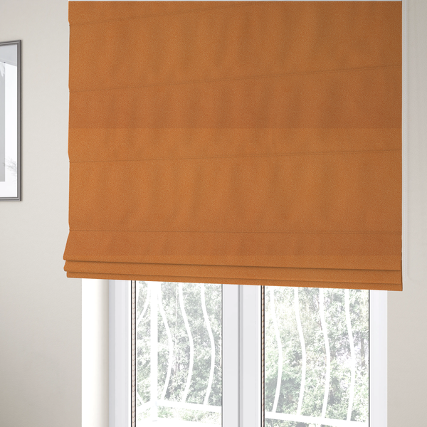 The fabric used to create these Roman blinds is a bright orange or tangerine Merida Suede upholstery fabric. The textile features a highly detailed, dense, and uniform embossed pebbled pattern, giving the soft suede material an intricate, tactile shagreen texture.