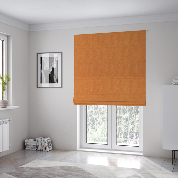 The fabric used to create these Roman blinds is a bright orange or tangerine Merida Suede upholstery fabric. The textile features a highly detailed, dense, and uniform embossed pebbled pattern, giving the soft suede material an intricate, tactile shagreen texture.