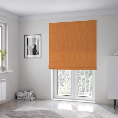 The fabric used to create these Roman blinds is a bright orange or tangerine Merida Suede upholstery fabric. The textile features a highly detailed, dense, and uniform embossed pebbled pattern, giving the soft suede material an intricate, tactile shagreen texture.