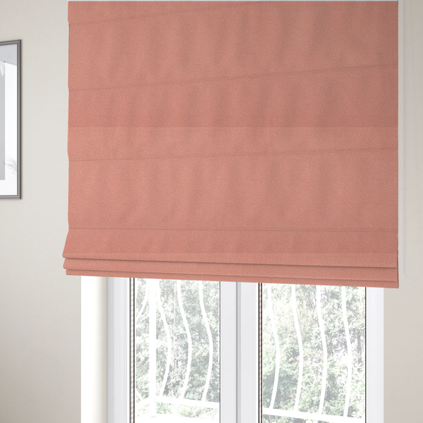 The fabric used to create these Roman blinds is a soft salmon pink or coral Merida Suede upholstery fabric. The textile features a highly detailed, dense, and uniform embossed pebbled pattern, giving the soft suede material an intricate, tactile shagreen texture.