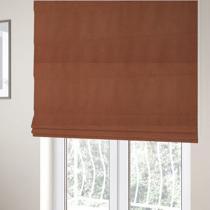 The fabric used to create these Roman blinds is a warm terracotta or rust orange Merida Suede upholstery fabric. The textile features a highly detailed, dense, and uniform embossed pebbled pattern, giving the soft suede material an intricate, tactile shagreen texture.