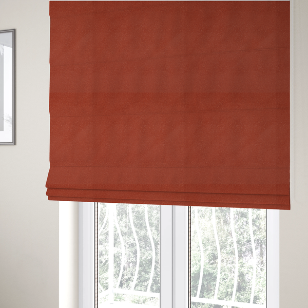The fabric used to create these Roman blinds is a vibrant brick red or rust Merida Suede upholstery fabric. The textile features a highly detailed, dense, and uniform embossed pebbled pattern, giving the soft suede material an intricate, tactile shagreen texture.