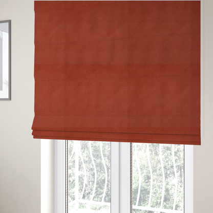 The fabric used to create these Roman blinds is a vibrant brick red or rust Merida Suede upholstery fabric. The textile features a highly detailed, dense, and uniform embossed pebbled pattern, giving the soft suede material an intricate, tactile shagreen texture.