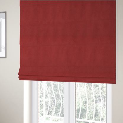 The fabric used to create these Roman blinds is a rich crimson or deep red Merida Suede upholstery fabric. The textile features a highly detailed, dense, and uniform embossed pebbled pattern, giving the soft suede material an intricate, tactile shagreen texture.