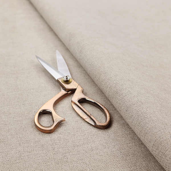 A finely textured weave in a soft greige or light stone shade. The material features a subtle heathered look with tiny flecks of pale grey, cream, and beige undertones throughout.