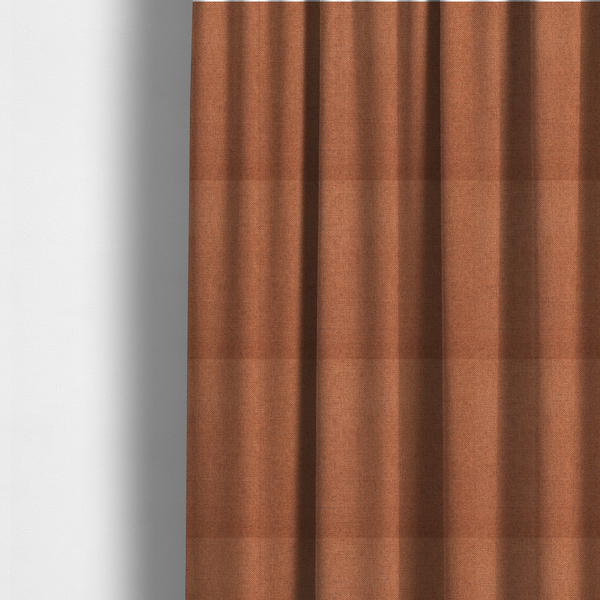 The fabric used to create these made-to-measure curtains is a finely textured weave in a bright ginger, amber, or light rust shade. The material features a subtle heathered look with finely blended threads of warm orange and darker neutral undertones throughout.