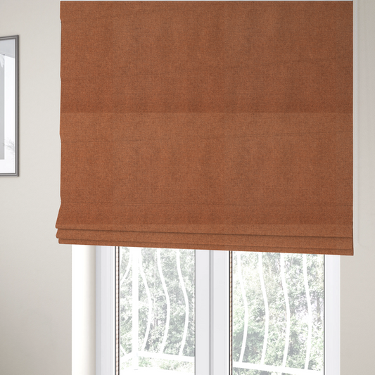 The fabric used to create these Roman blinds is a finely textured weave in a bright ginger, amber, or light rust shade. The material features a subtle heathered look with finely blended threads of warm orange and darker neutral undertones throughout.