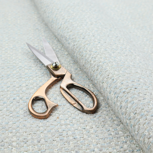 The material features a dense, light-toned weave with a pale cream and off-white base, subtly interlaced with delicate horizontal flecks of soft baby blue and light grey threads throughout.