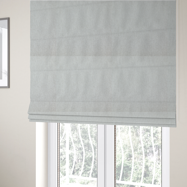 The fabric used to create these Roman blinds is a lightly textured upholstery fabric in a pale cream or light grey. The material features a fine, tight weave with faint horizontal striations and a matte finish.