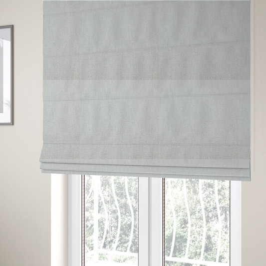 The fabric used to create these Roman blinds is a lightly textured upholstery fabric in a pale cream or light grey. The material features a fine, tight weave with faint horizontal striations and a matte finish.