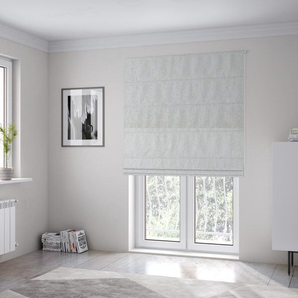 The fabric used to create these Roman blinds is a lightly textured upholstery fabric in a pale cream or light grey. The material features a fine, tight weave with faint horizontal striations and a matte finish.